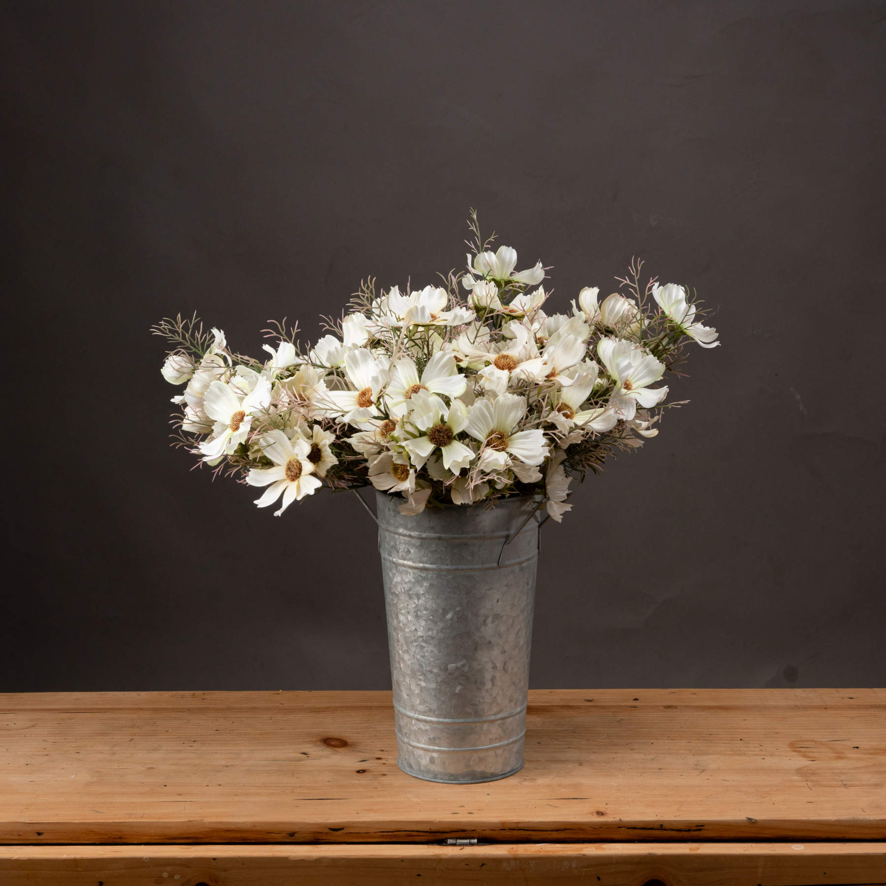 Cream cosmos spray in a galvanized bucket, featuring soft cream petals and wispy greenery, enhances any decor with elegance.