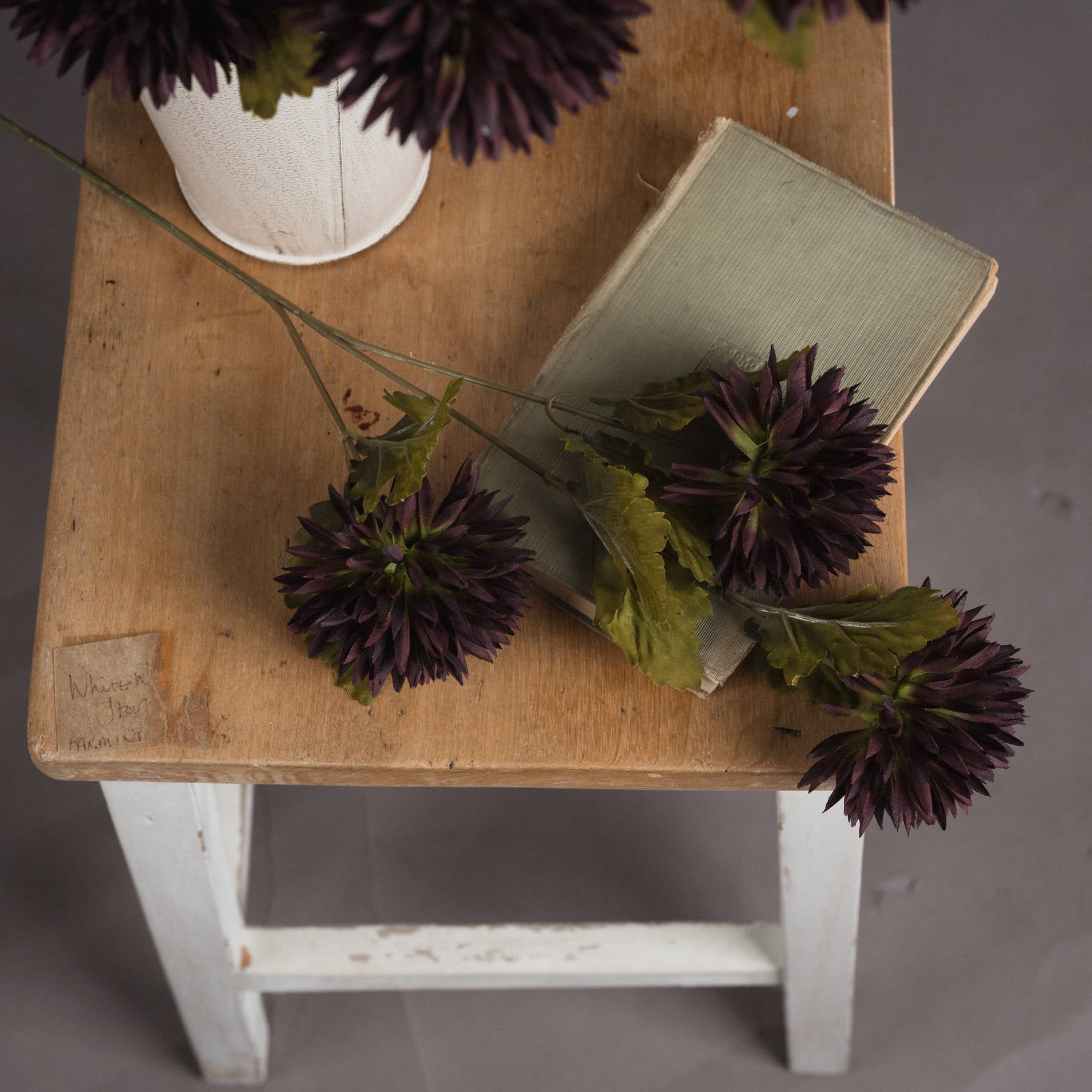 Deep chocolate chrysanthemum stems with curling petals and green foliage arranged on a wooden table with a book.