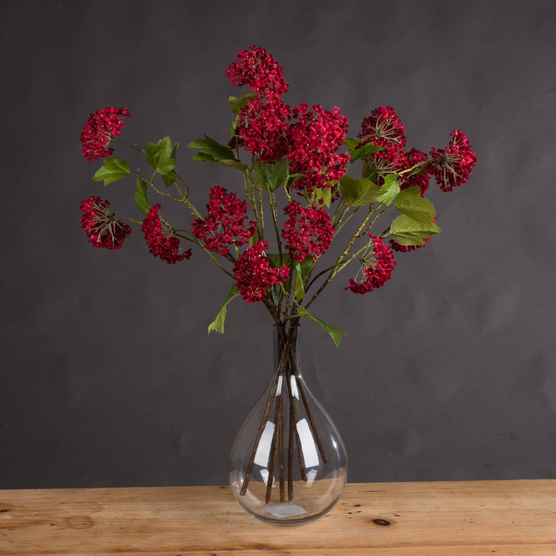 Vibrant red artificial viburnum stems in a clear vase, featuring densely clustered berries and green leaves, perfect for autumn decor.