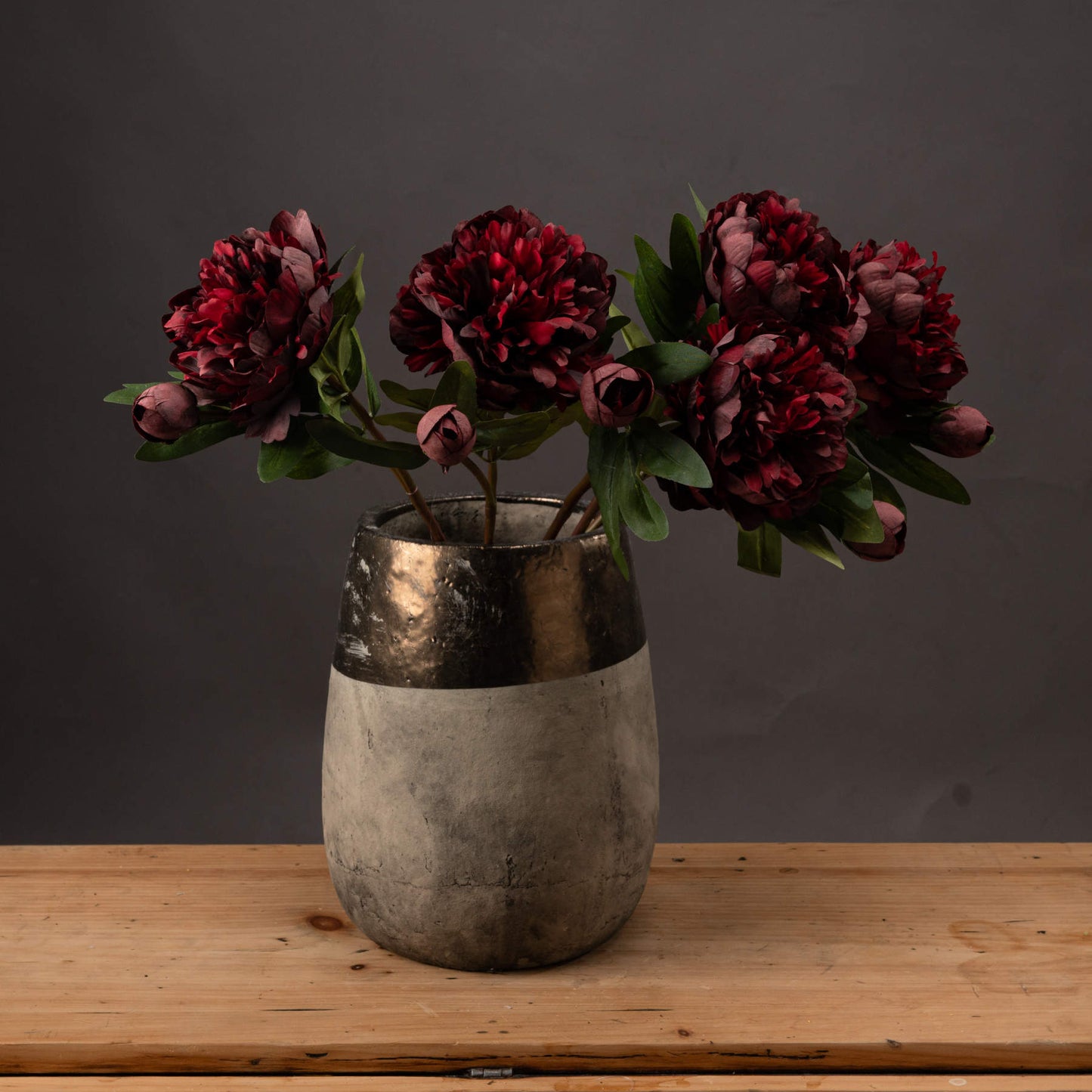 Luxurious burgundy peony roses in a sleek, metallic vase; rich tones and intricate details add elegance to any decor.