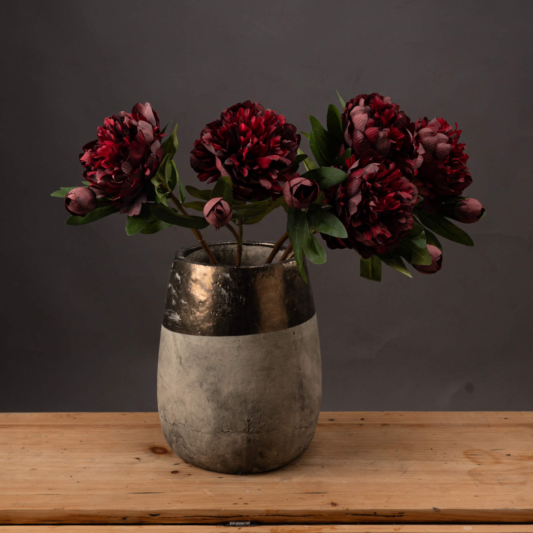 Luxurious burgundy peony roses in a sleek, metallic vase; rich tones and intricate details add elegance to any decor.