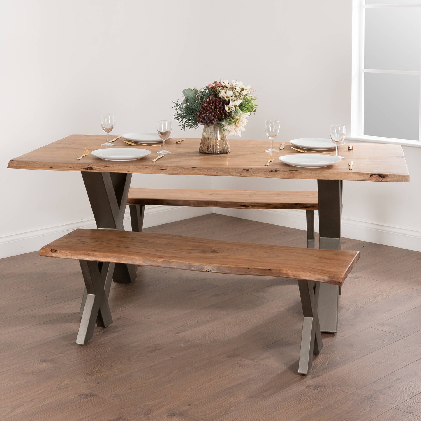 Live edge dining table of Indian acacia with natural contours, supported by a sleek grey metal frame, complemented by a simple bench.