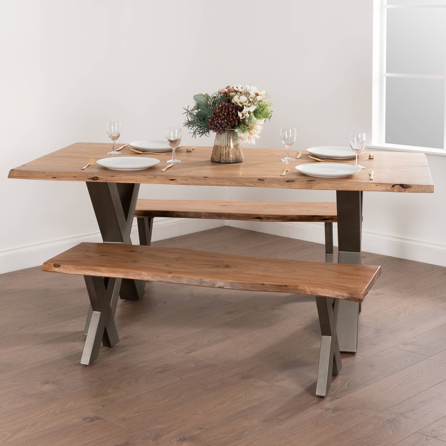 Live edge dining table of Indian acacia with natural contours, supported by a sleek grey metal frame, complemented by a simple bench.