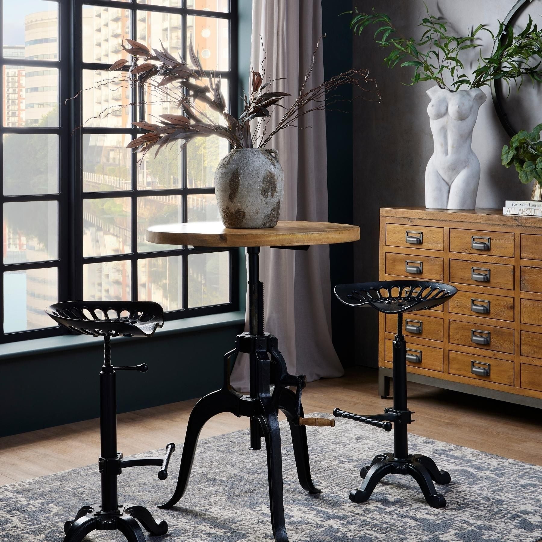 Industrial-style adjustable bar table with a weathered wood top, sturdy black metal frame, and two matching stools in a stylish setting.