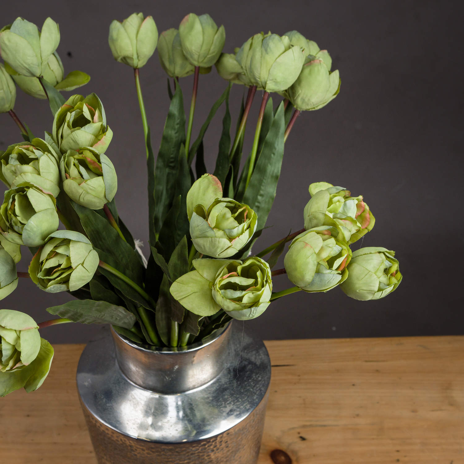 Realistic green tulips with soft petals and lush leaves arranged in a silver vase, creating an elegant decor piece.