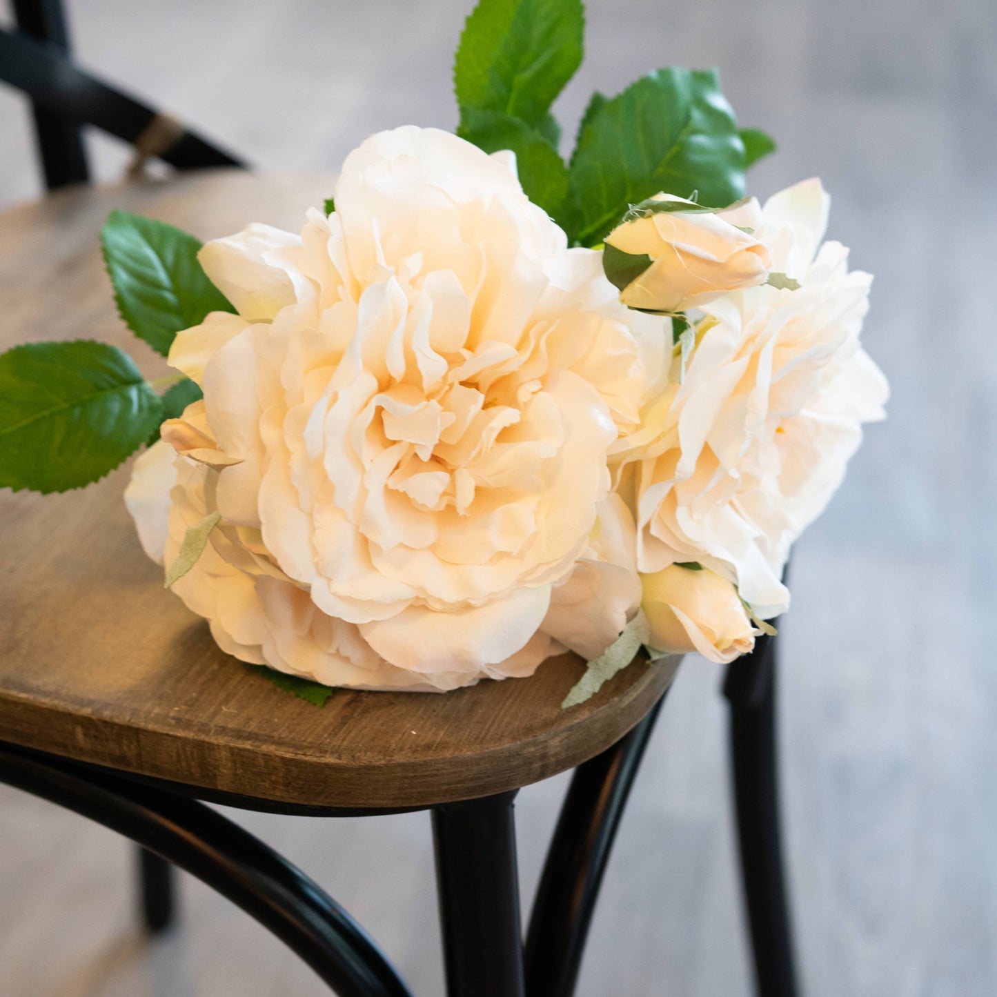 Peachy cream artificial rose bouquet with lush green leaves, elegantly arranged on a wooden surface, perfect for decor.