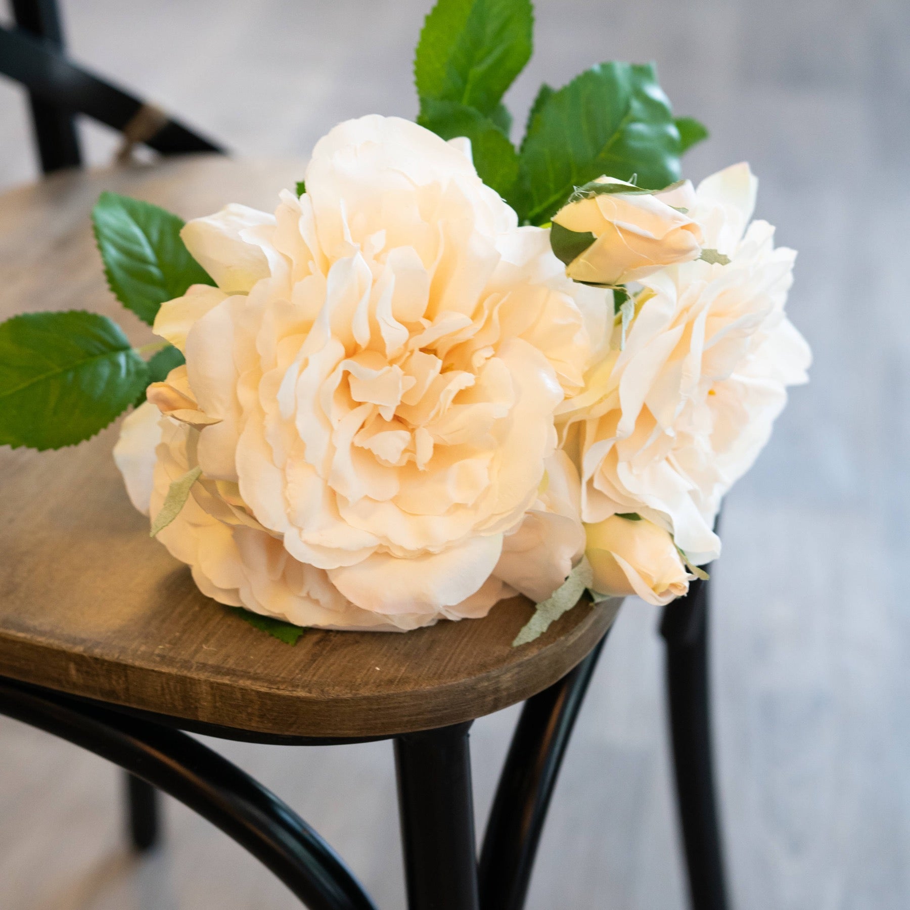 Peachy cream artificial rose bouquet with lush green leaves, elegantly arranged on a wooden surface, perfect for decor.
