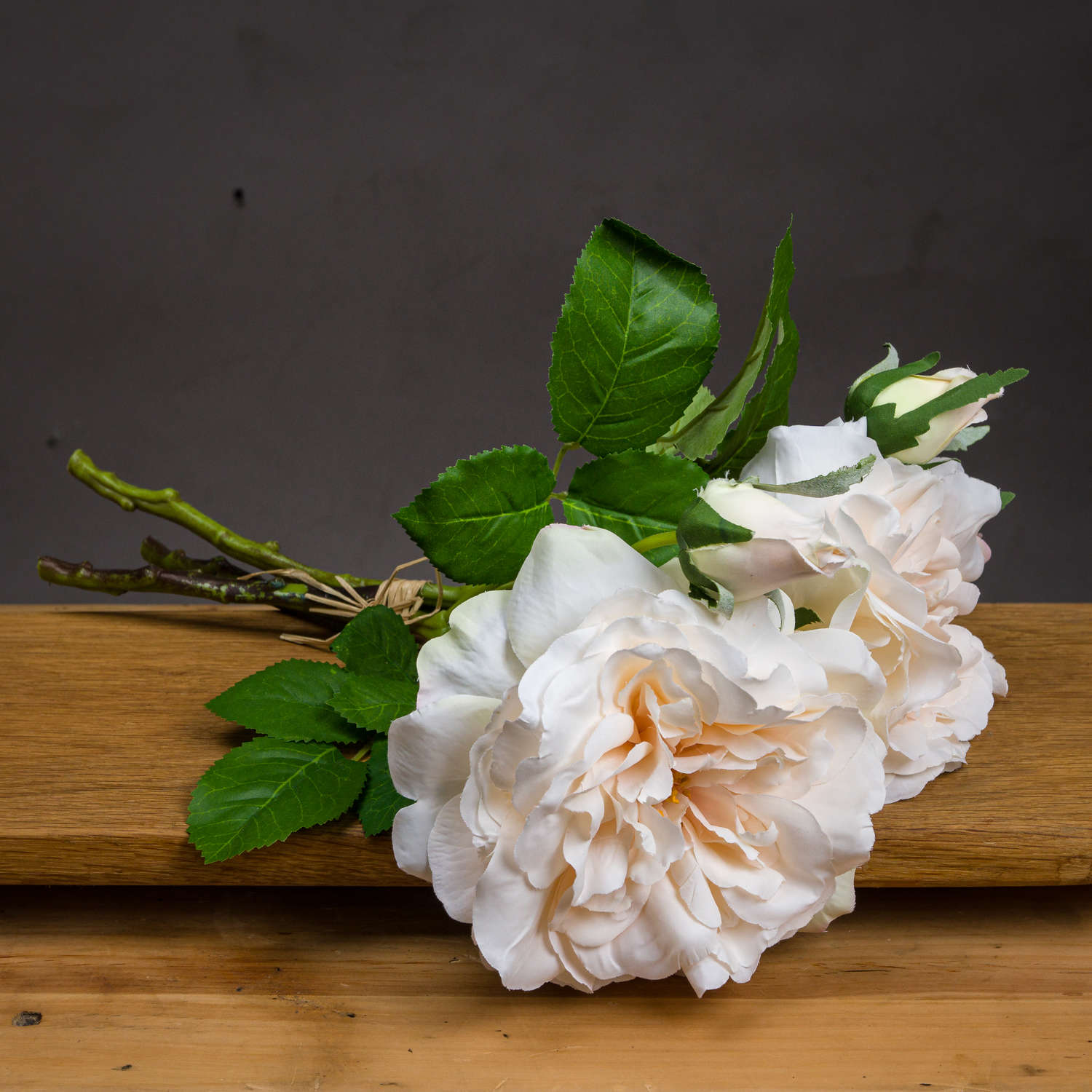 Peachy cream rose bouquet with lush green leaves, tied with rustic twine, resting on a wooden surface. Elegant and versatile decor.