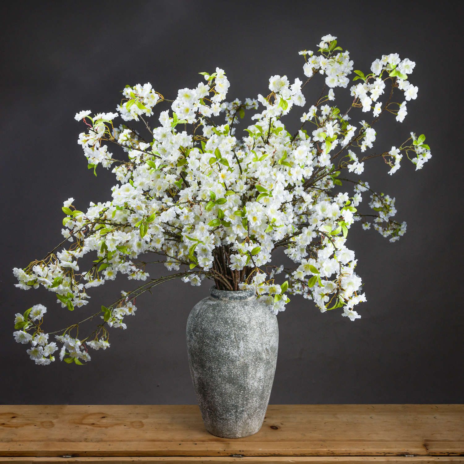 Lifelike white cherry blossom spray in a textured gray vase, showcasing full clusters and delicate green accents, perfect for elegant decor.