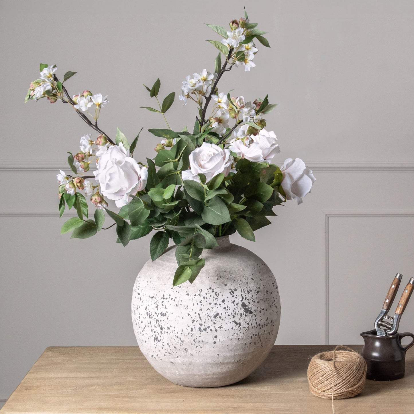 Artificial pastel pink blossoms and green leaves in a textured gray vase, enhancing springtime decor with elegance.