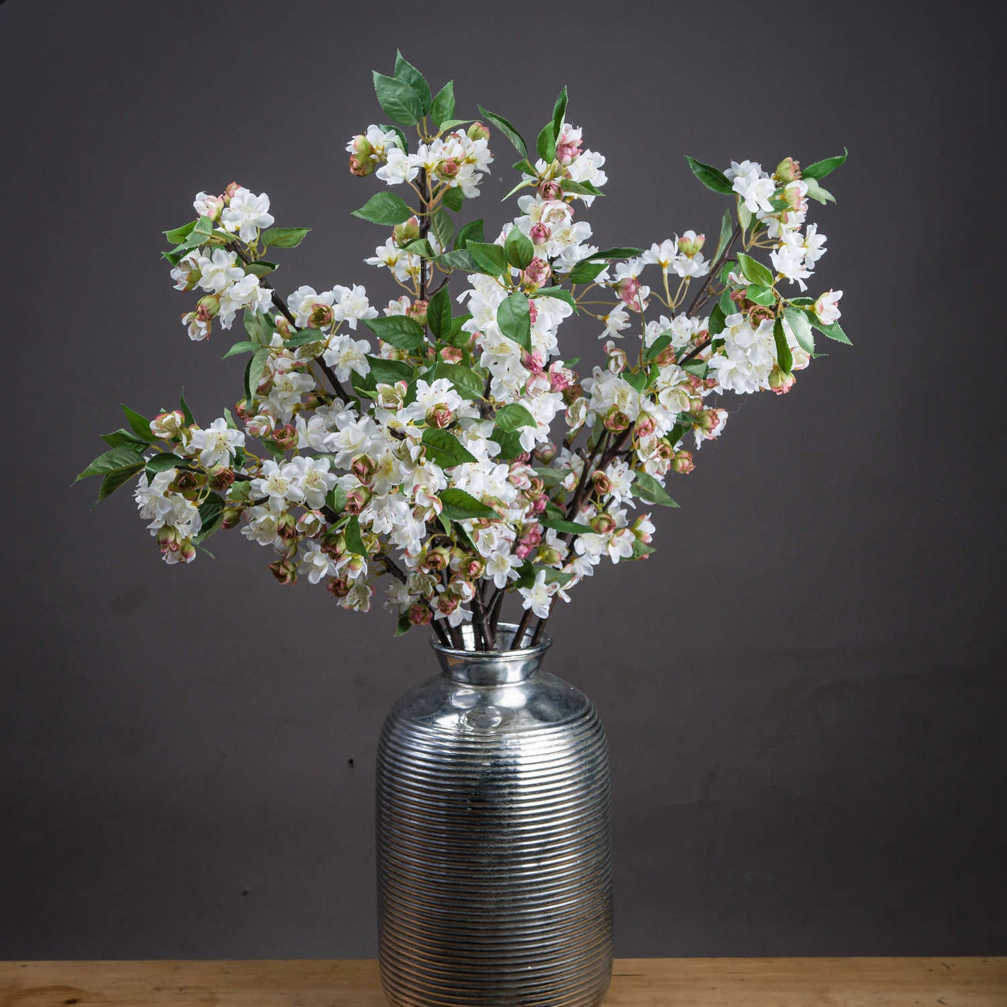 Pale pink blossoms and vibrant green leaves on elegant stems, displayed in a silver textural vase, exuding springtime charm.