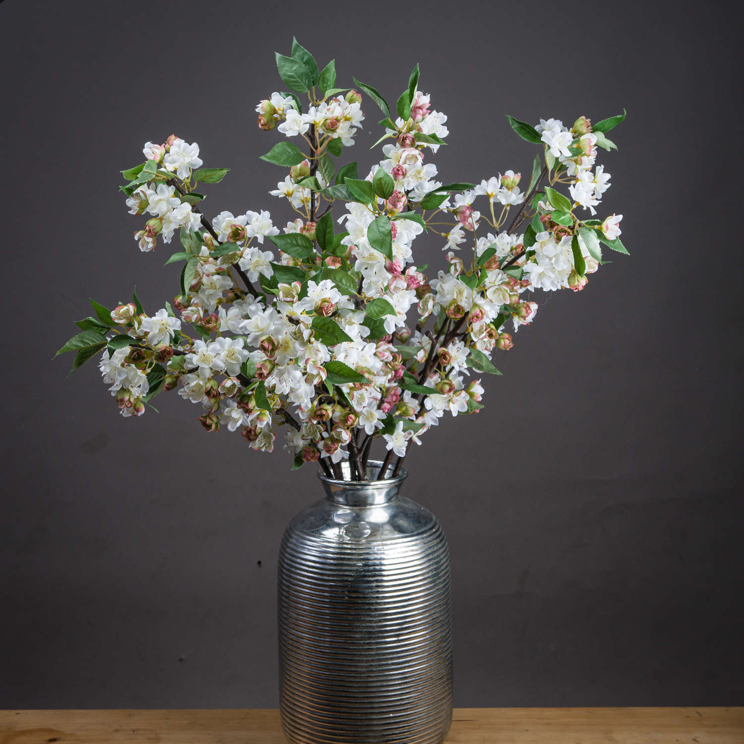 Pale pink blossoms and vibrant green leaves on elegant stems, displayed in a silver textural vase, exuding springtime charm.