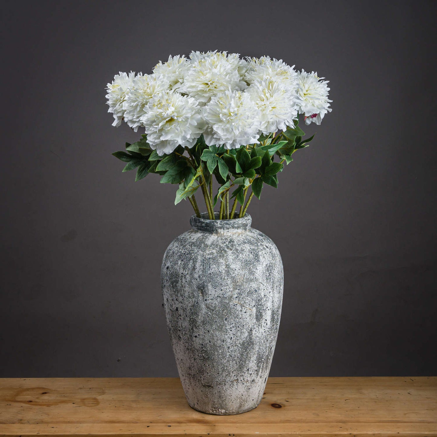 Artificial white peony bouquet in a textured gray vase, featuring detailed petals and greenery for elegant home decor.
