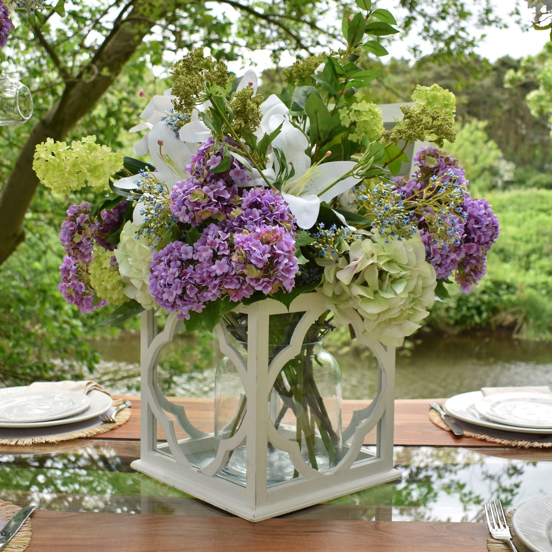 Elegant arrangement of artificial cream gardenia and mixed flowers in a white lantern vase, enhancing a serene outdoor setting.