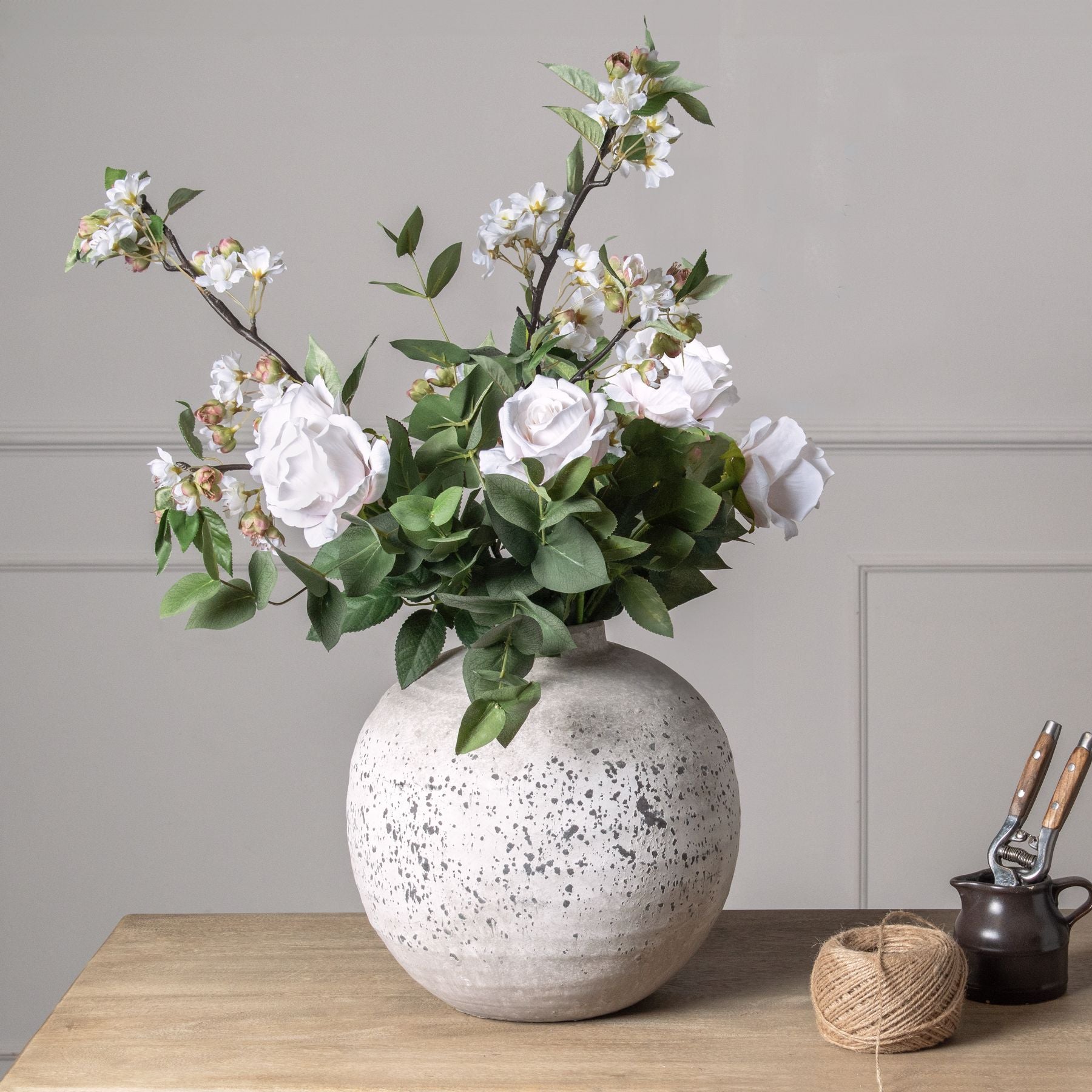 Pastel pink tea rose with lifelike petals and greenery in a speckled vase, complementing a chic wooden table setting.