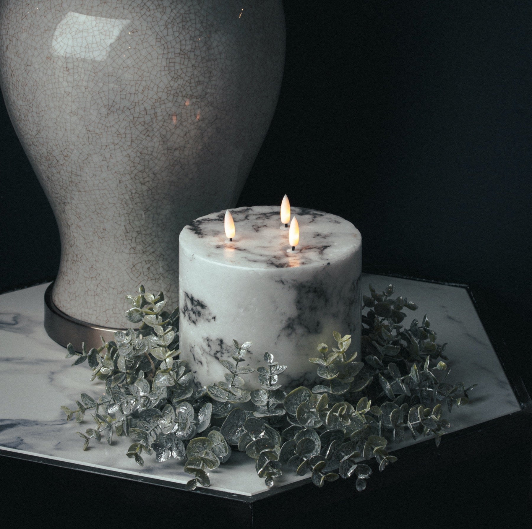 White marble-effect LED candle with three realistic amber flames, surrounded by silver foliage, enhancing a sophisticated ambiance.