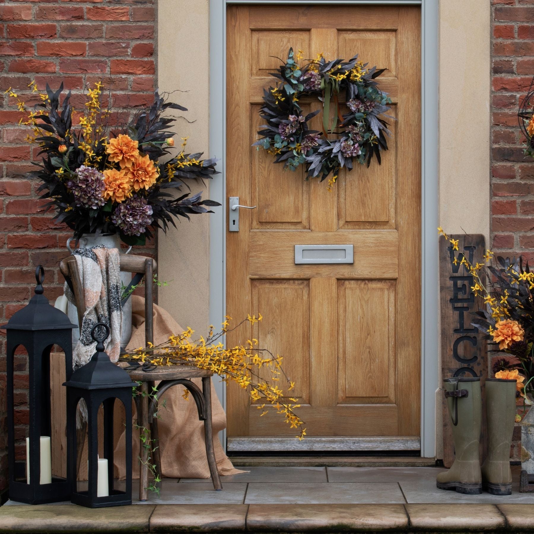 Vibrant orange dahlia spray accented with dark leaves, enhancing autumn decor against a rustic door backdrop.