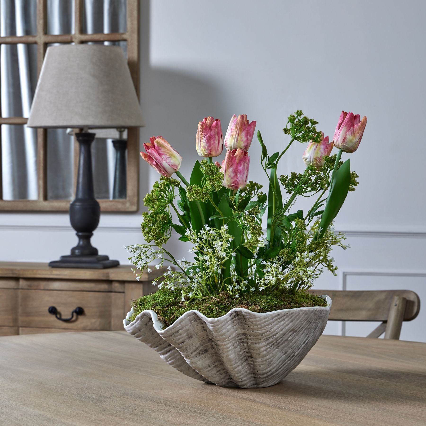 Elegant arrangement featuring pink and white flowers with greenery in a textured shell-shaped vase, set against a neutral backdrop.