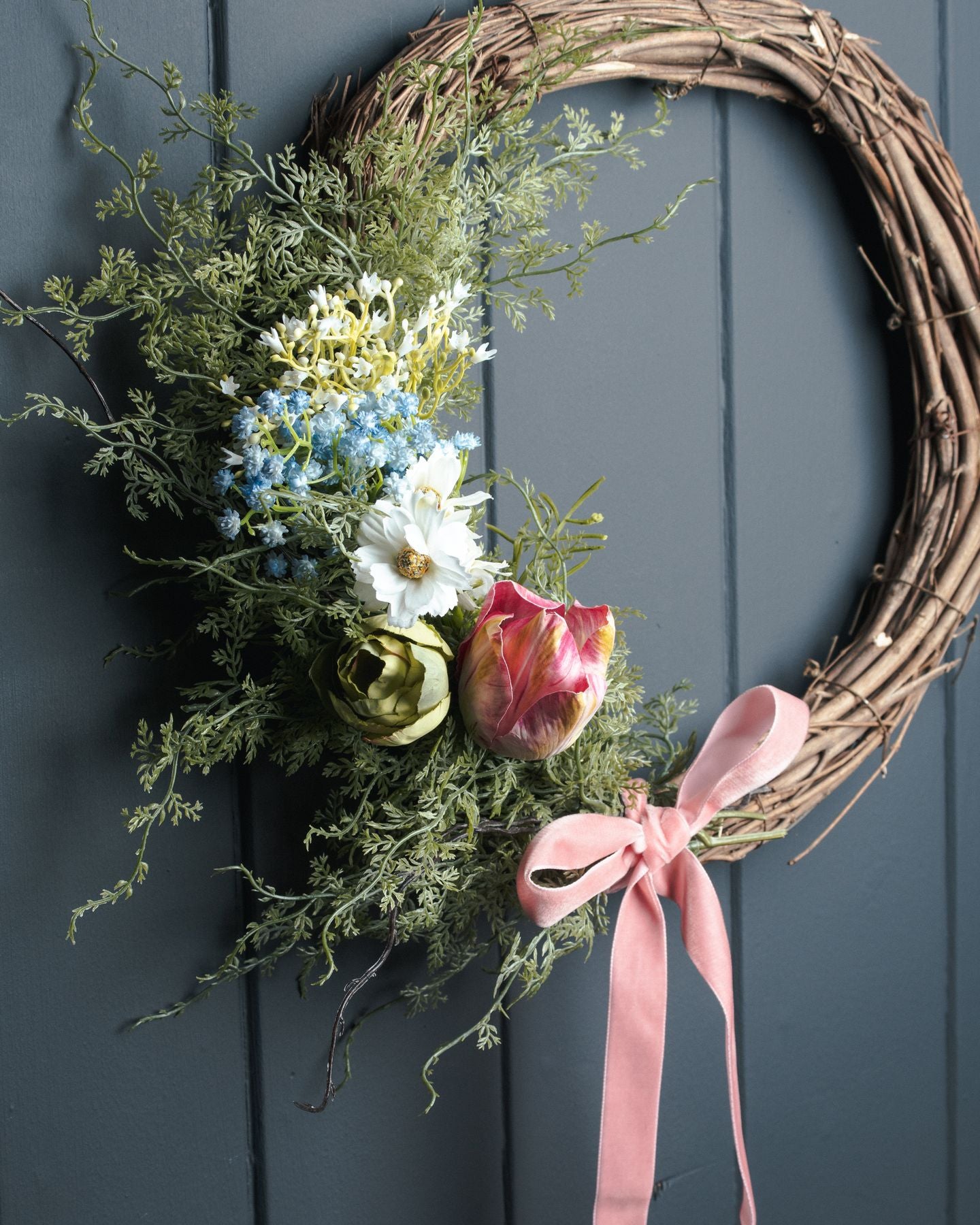 Vibrant faux asparagus fern bunch with lush green fronds, complemented by pastel flowers and a soft pink ribbon on a natural wreath.