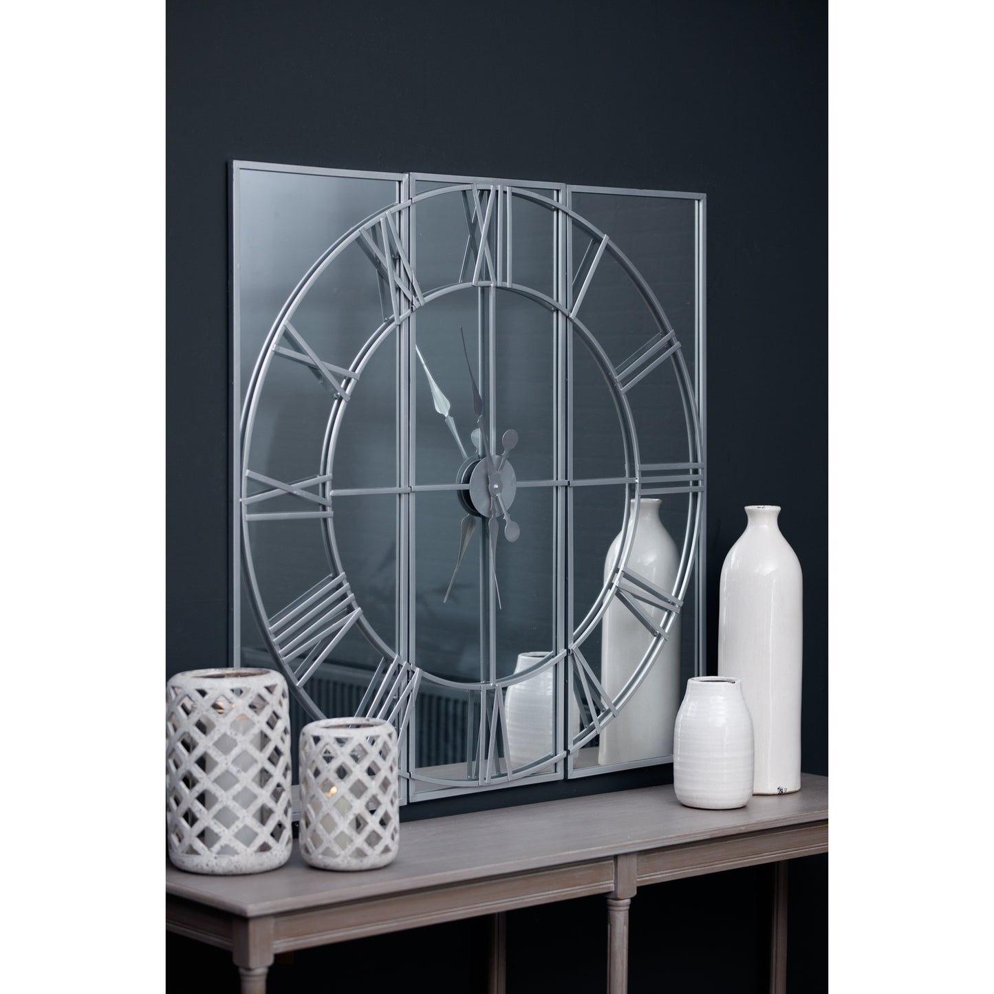 Sophisticated mirrored wall clock featuring a three-panel design with sleek metalwork, complemented by elegant white vases.