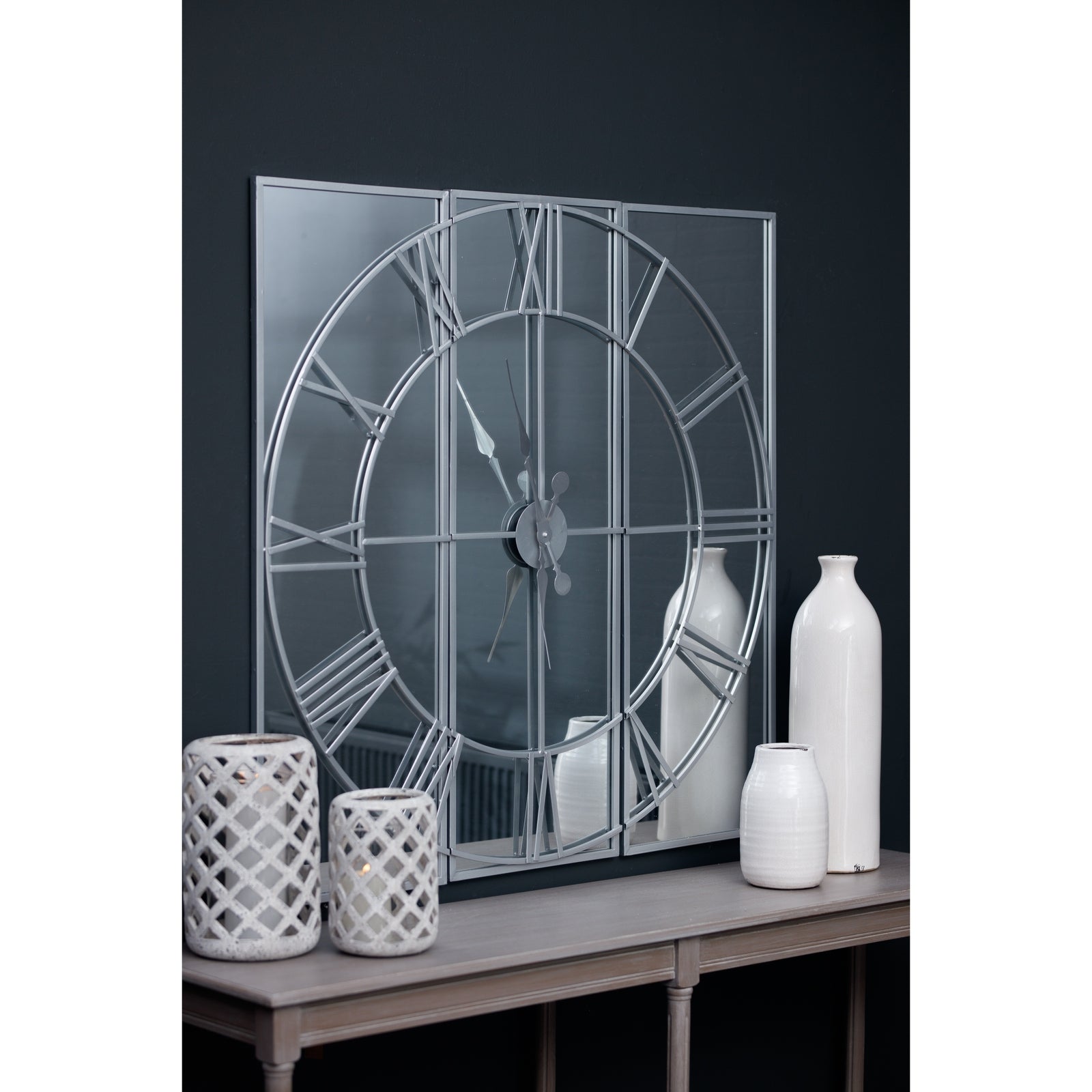 Sophisticated mirrored wall clock featuring a three-panel design with sleek metalwork, complemented by elegant white vases.