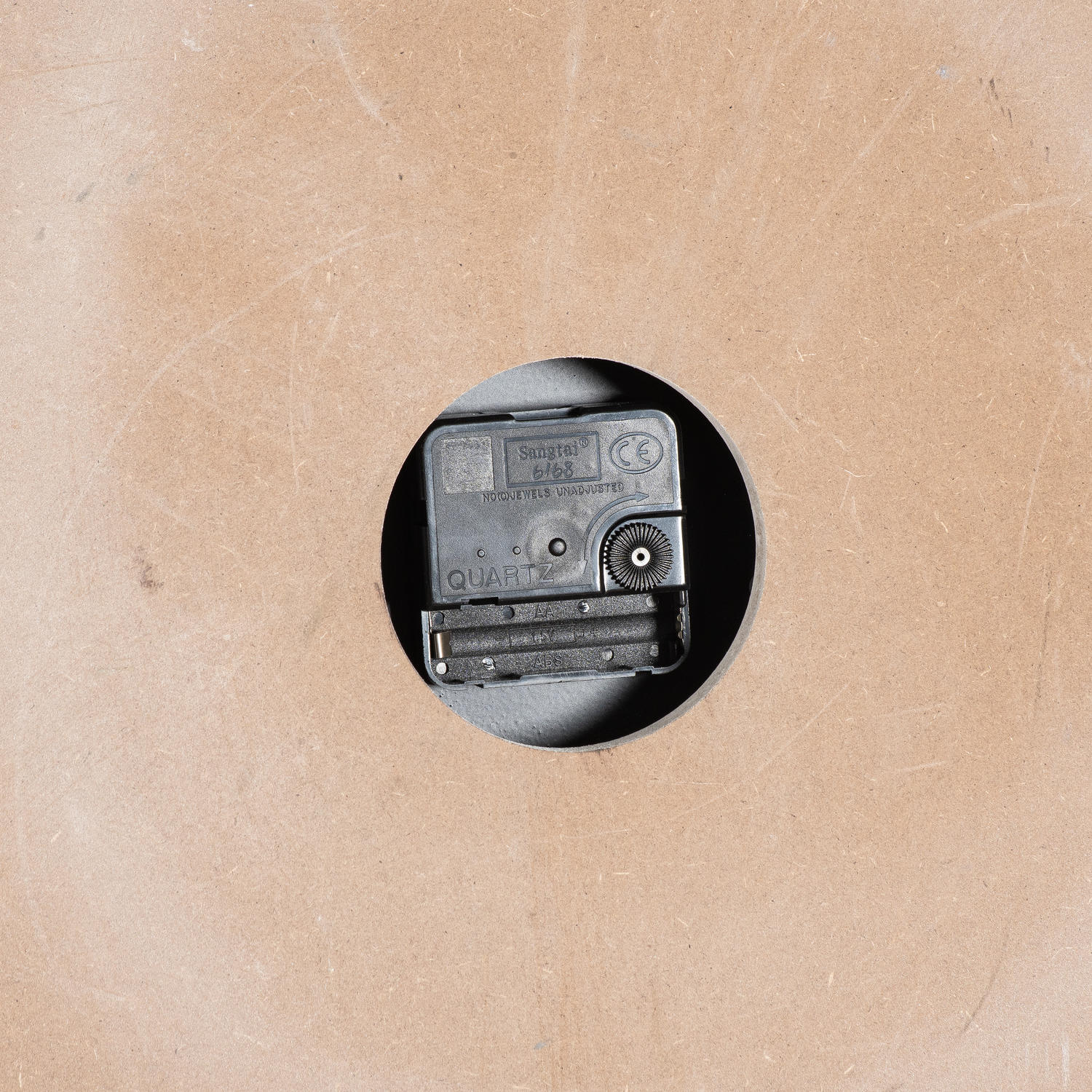 Quartz clock mechanism mounted on a beige backing, featuring a circular cutout for wall display.
