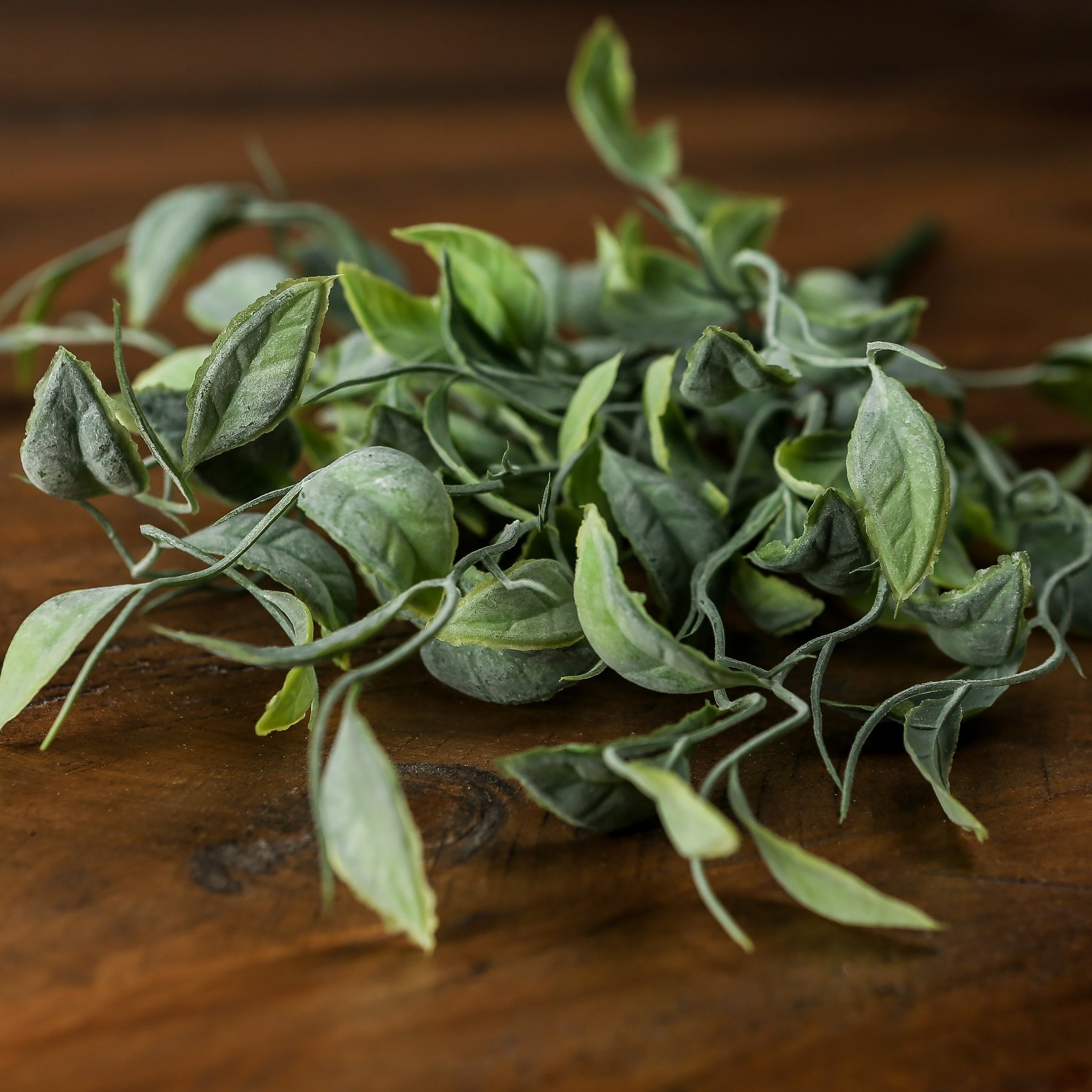 Lifelike green foliage with varied shades and organic movement, resting on a wooden surface, perfect for home decor.