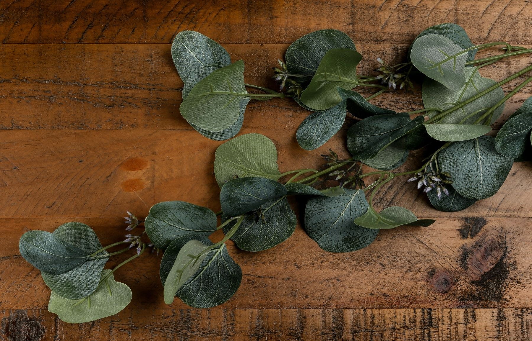 Realistic green eucalyptus stem spray arranged on a wooden surface, featuring lush leaves and subtle floral accents, perfect for decor.