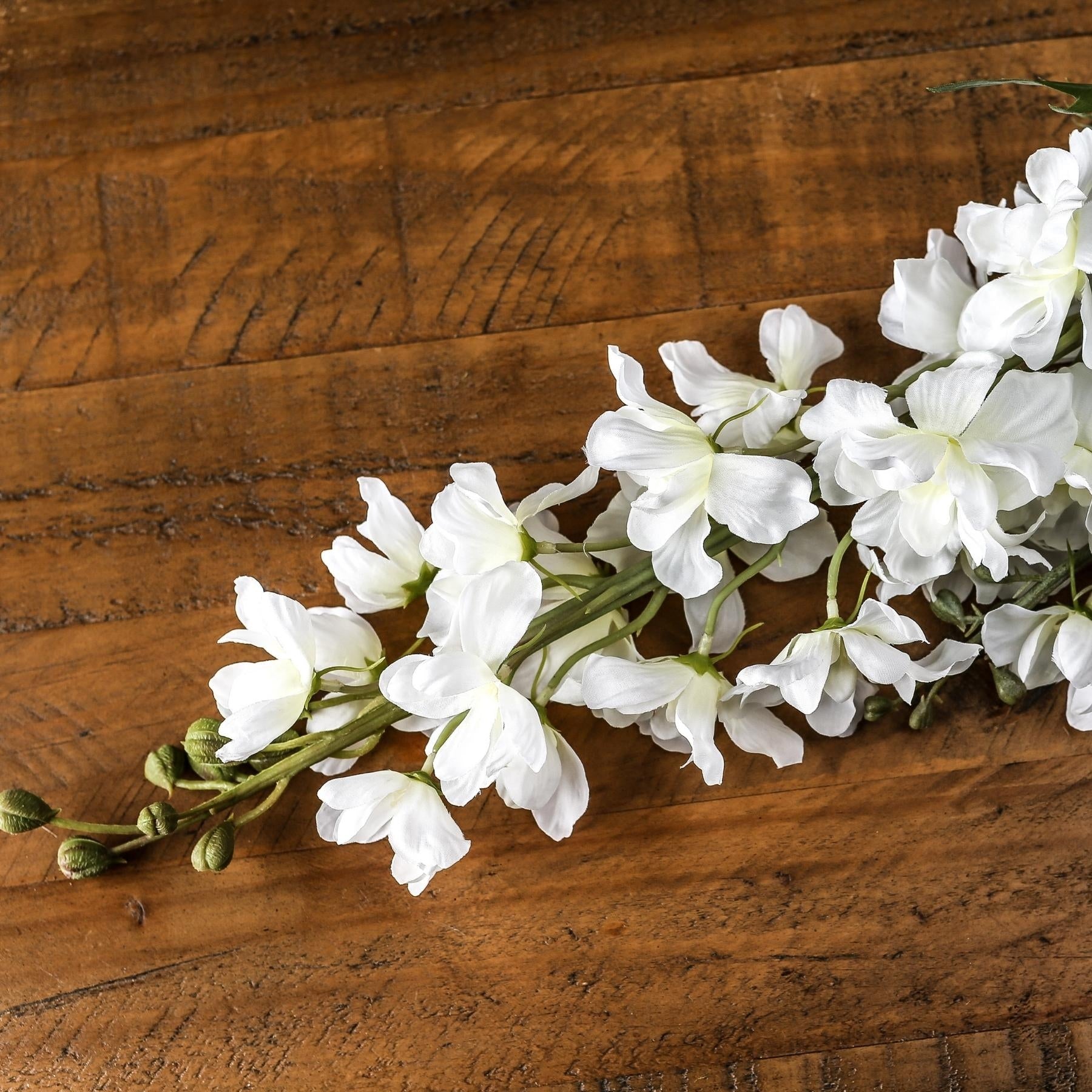 Elegant tall white delphinium stem with lifelike florets and green buds, laid on a rustic wooden surface.