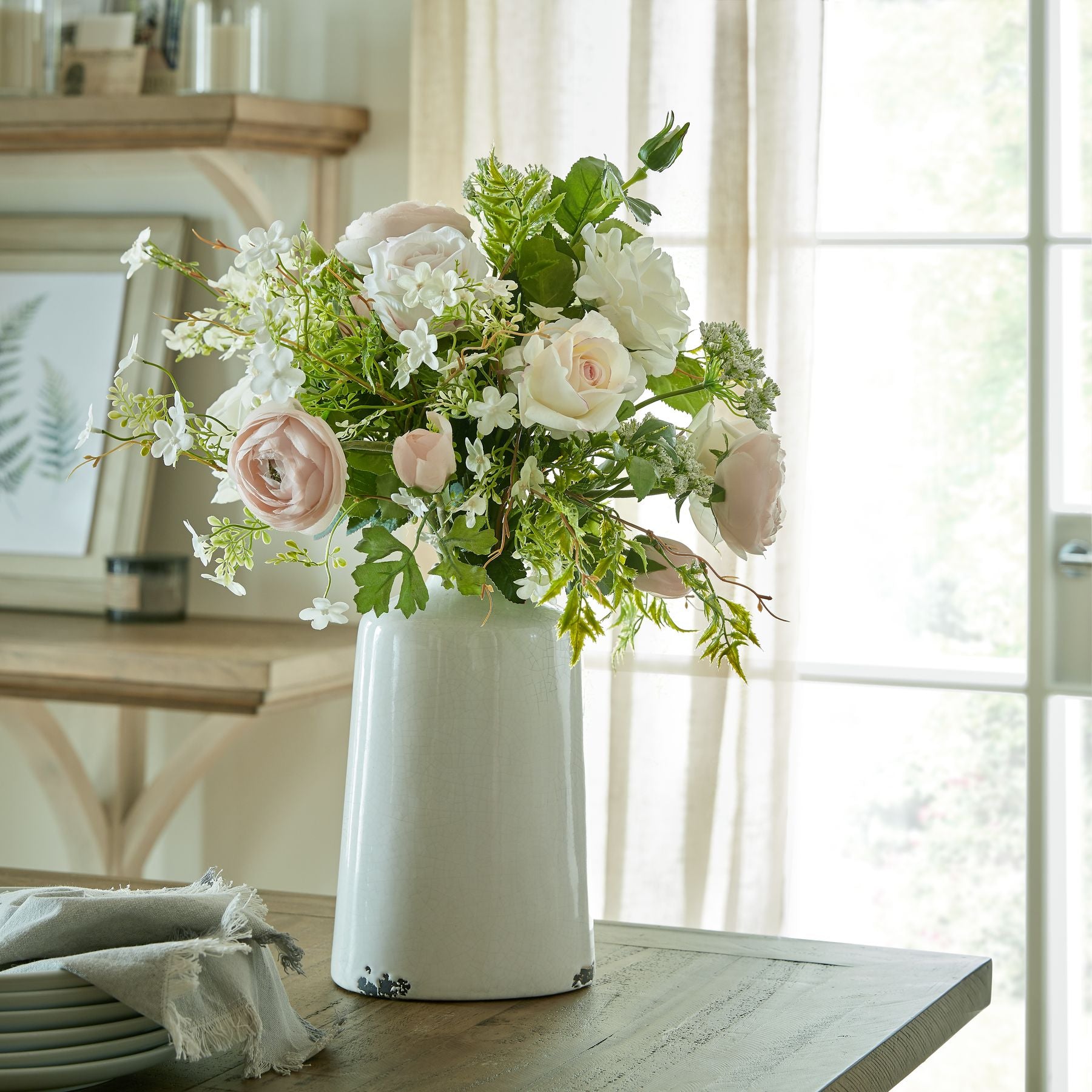 Delicate white bellflower blooms elegantly alongside soft pink roses and greenery in a sleek white vase, enhancing a serene ambiance.