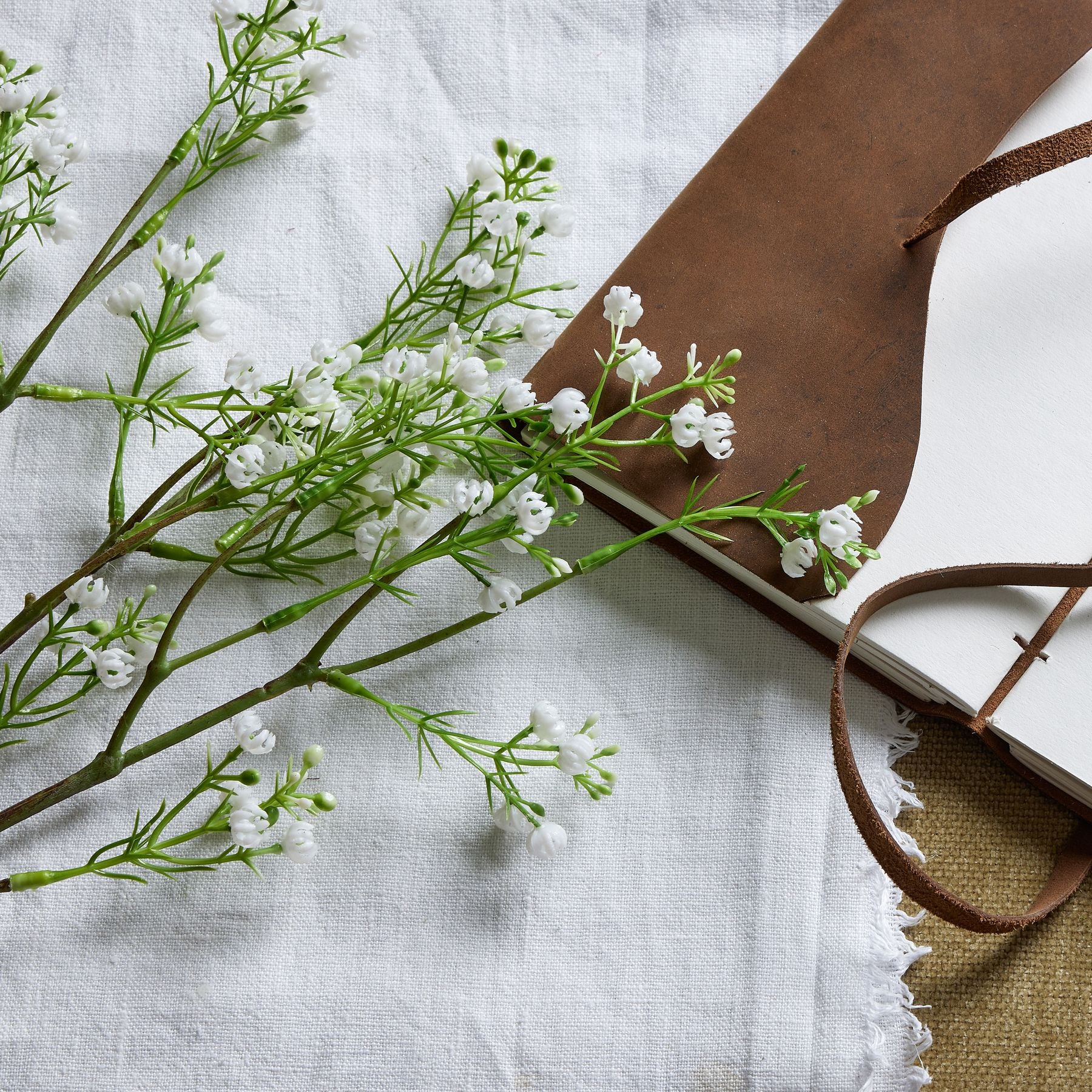 Lifelike artificial Lily of the Valley stem with delicate white blossoms and lush green foliage, resting on textured fabric.