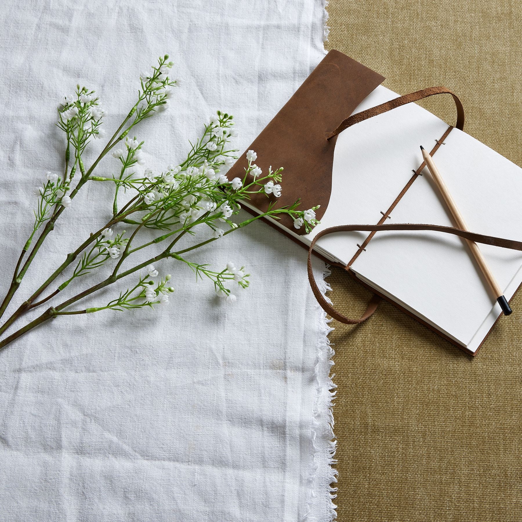 Artificial Lily of the Valley with delicate white blossoms and green stems, placed beside a brown notebook and pencil on a textured surface.