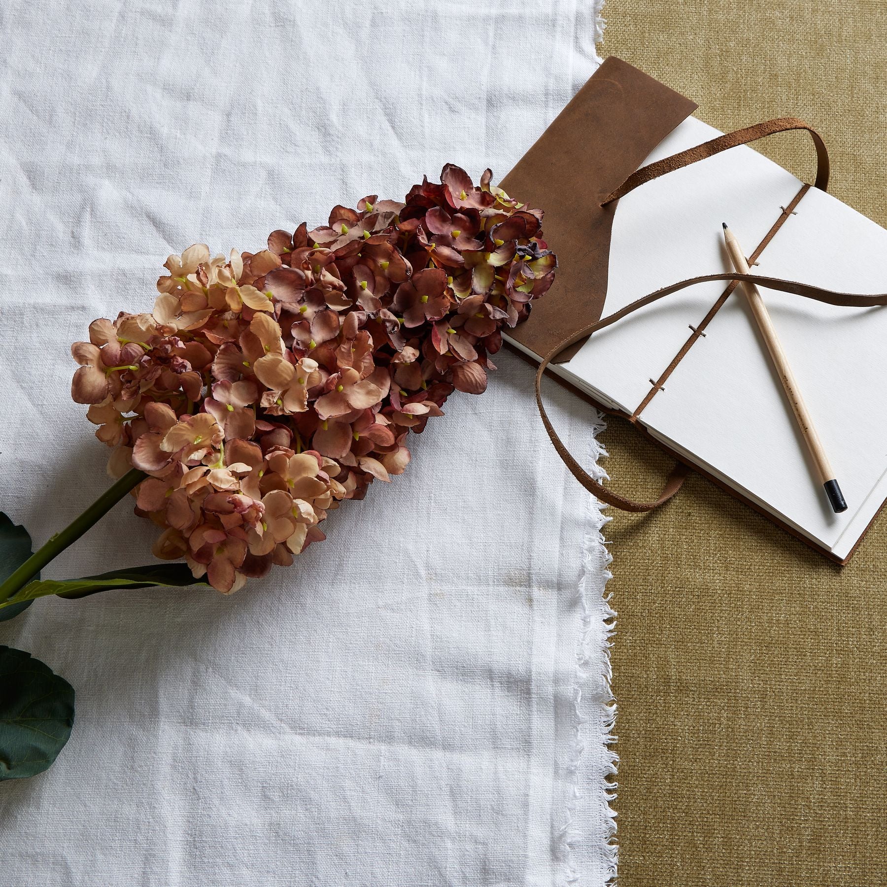 Burgundy Spear Hydrangea with deep burgundy petals and lush greenery, set on a textured fabric backdrop beside a notebook and pencil.