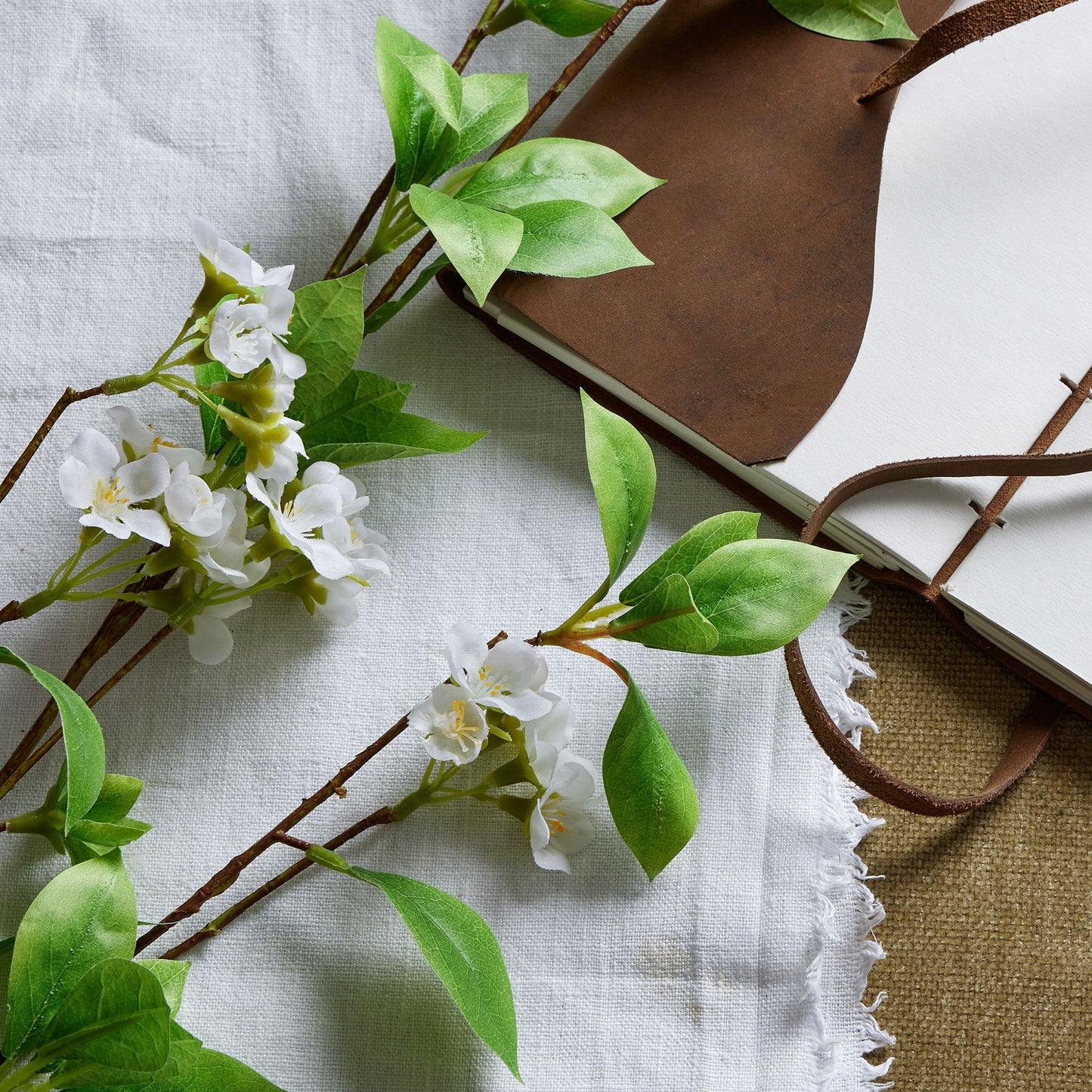 Tall mock orange spray featuring glossy green leaves and delicate white petals, set against a textured background.