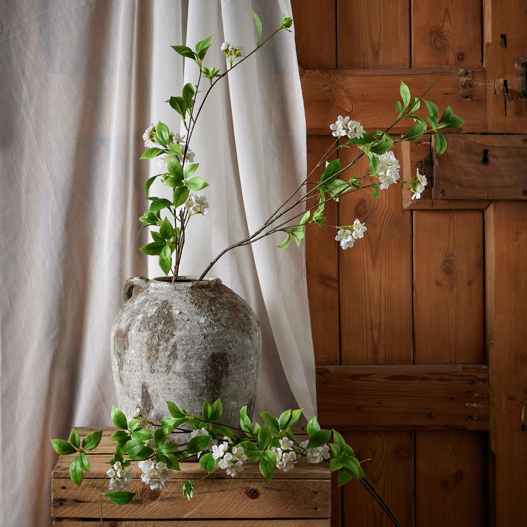 Tall mock orange spray features delicate white petals and glossy green leaves in a textured gray vase, enhancing elegant decor.