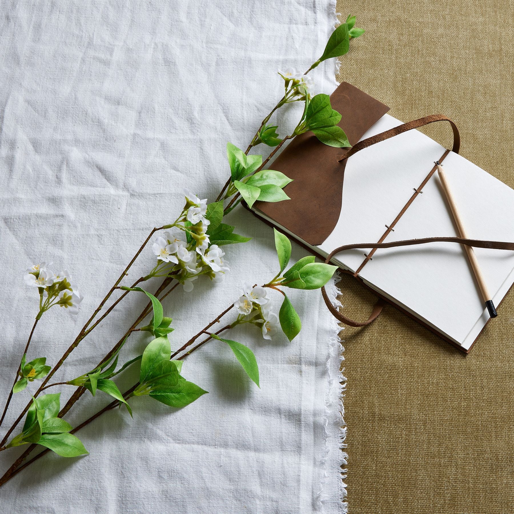 Tall mock orange spray featuring glossy green leaves and delicate white petals, elegantly arranged with a notebook and pen.