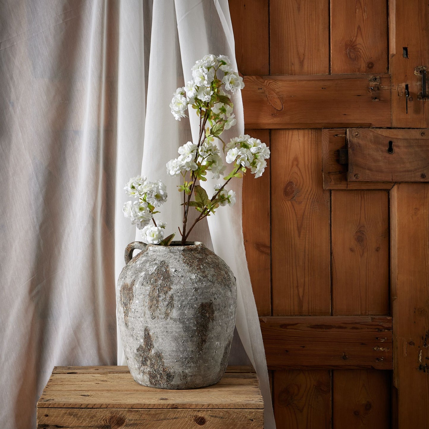 Tall white artificial flowers in a rustic gray vase, adding elegance to a wooden backdrop, enhancing any room's decor.