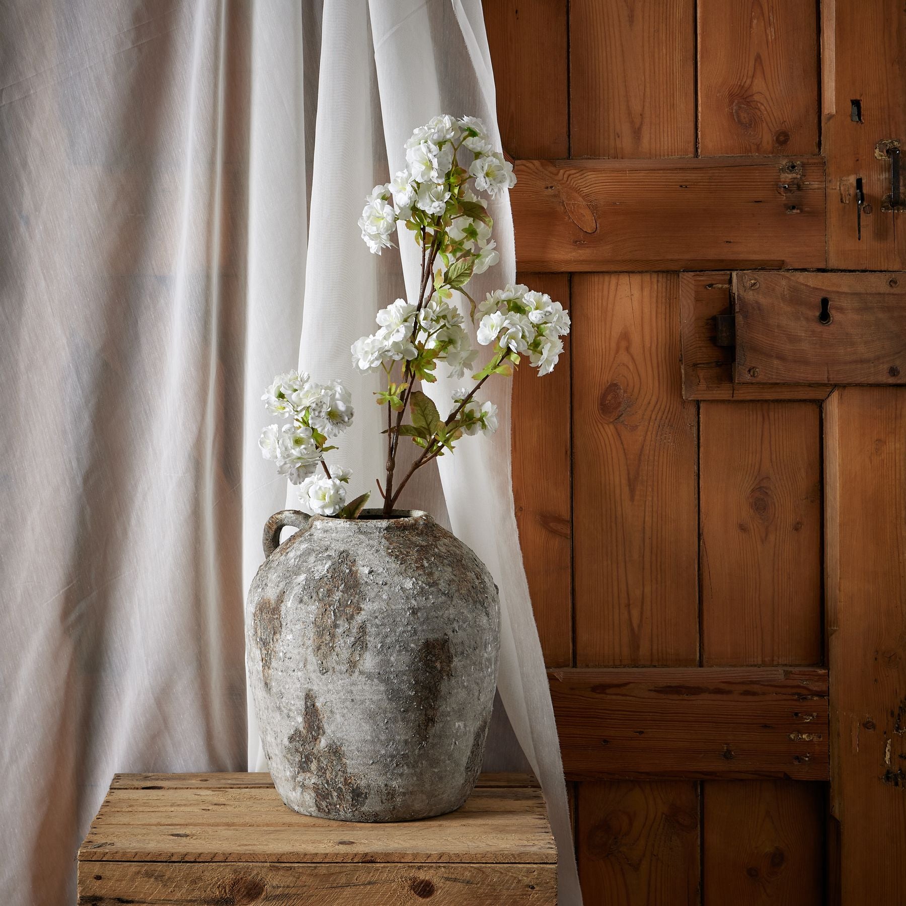 Tall white artificial flowers in a rustic gray vase, adding elegance to a wooden backdrop, enhancing any room's decor.