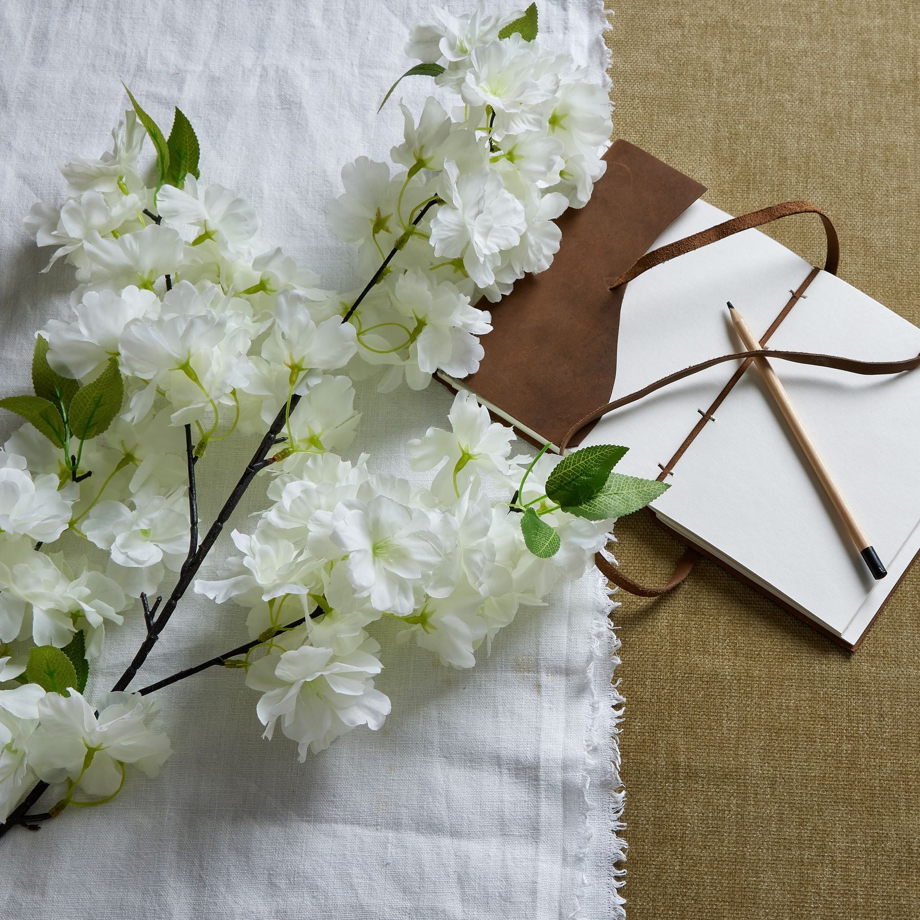 Large white cherry blossom stem with lifelike petals, elegantly cascading alongside a notebook and pencil on a textured background.