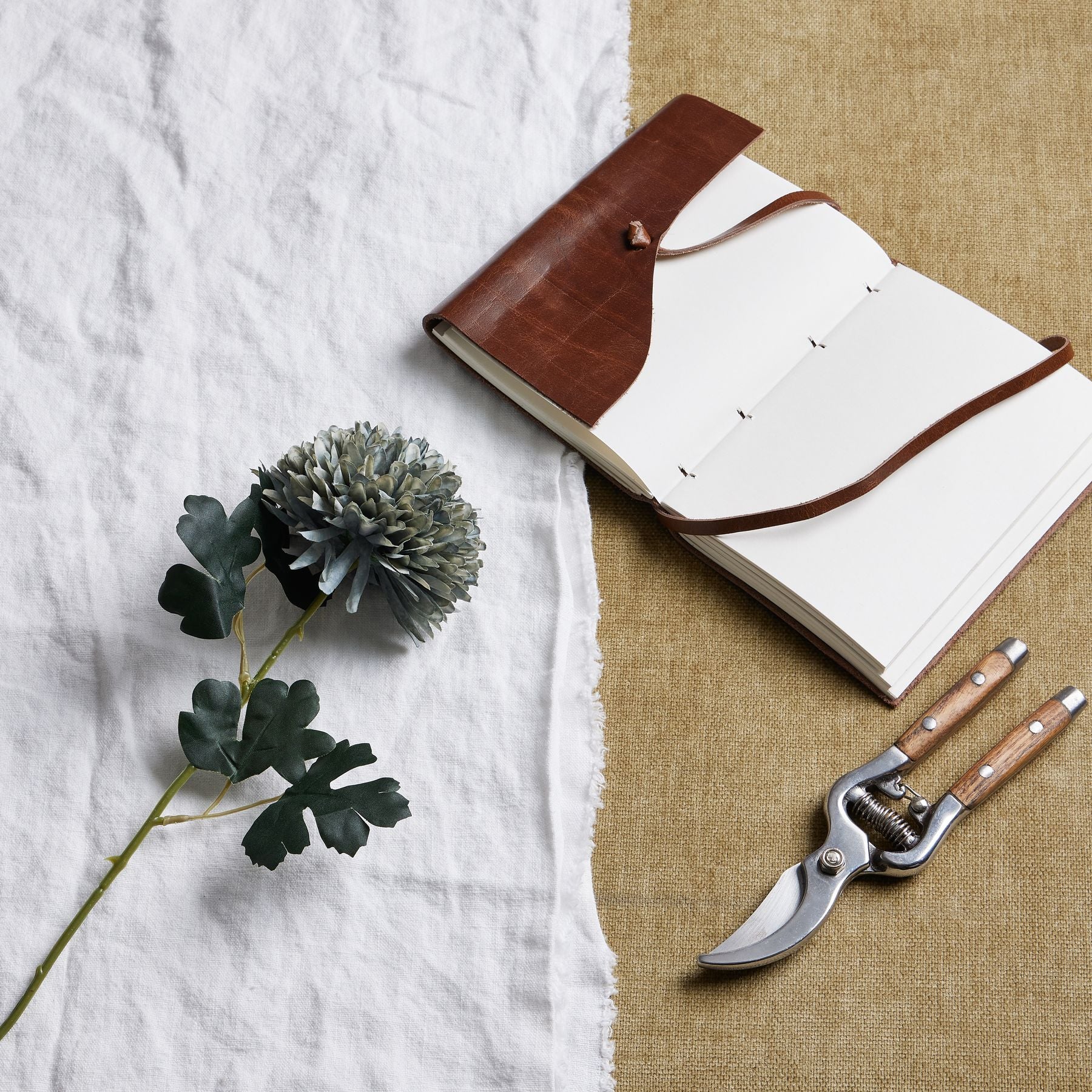 Pale green-blue chrysanthemum with textured petals rests beside a notebook and pruning shears, enhancing a serene, elegant setting.