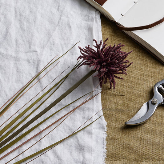 Burgundy Aster Spider Chrysanthemum stem with layered petals, set against textured fabric and tools, exuding autumn elegance.