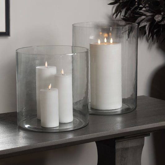 Clear glass cylinder vases with white candles inside, adding elegance to a neutral-toned tabletop. Ideal for versatile decor.