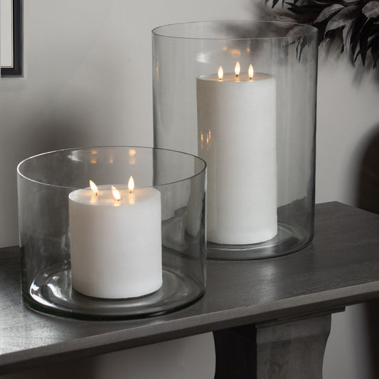 Clear glass vases in varying heights, each housing a white candle, create a warm and inviting ambiance on a dark wood surface.