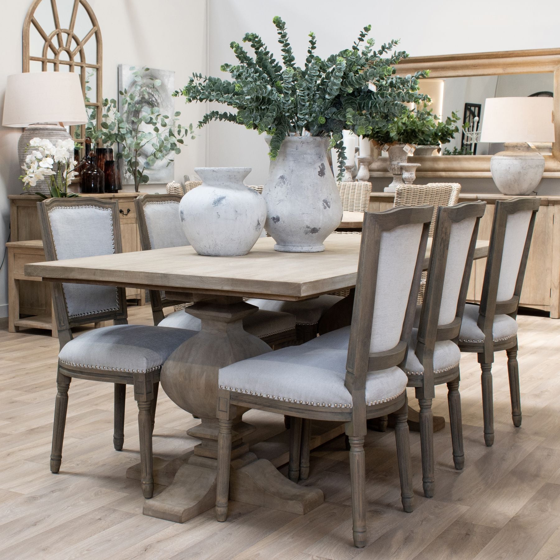 Large dining table featuring a washed hardwood finish, industrial black iron accents, and elegant upholstered chairs in a refined setting.