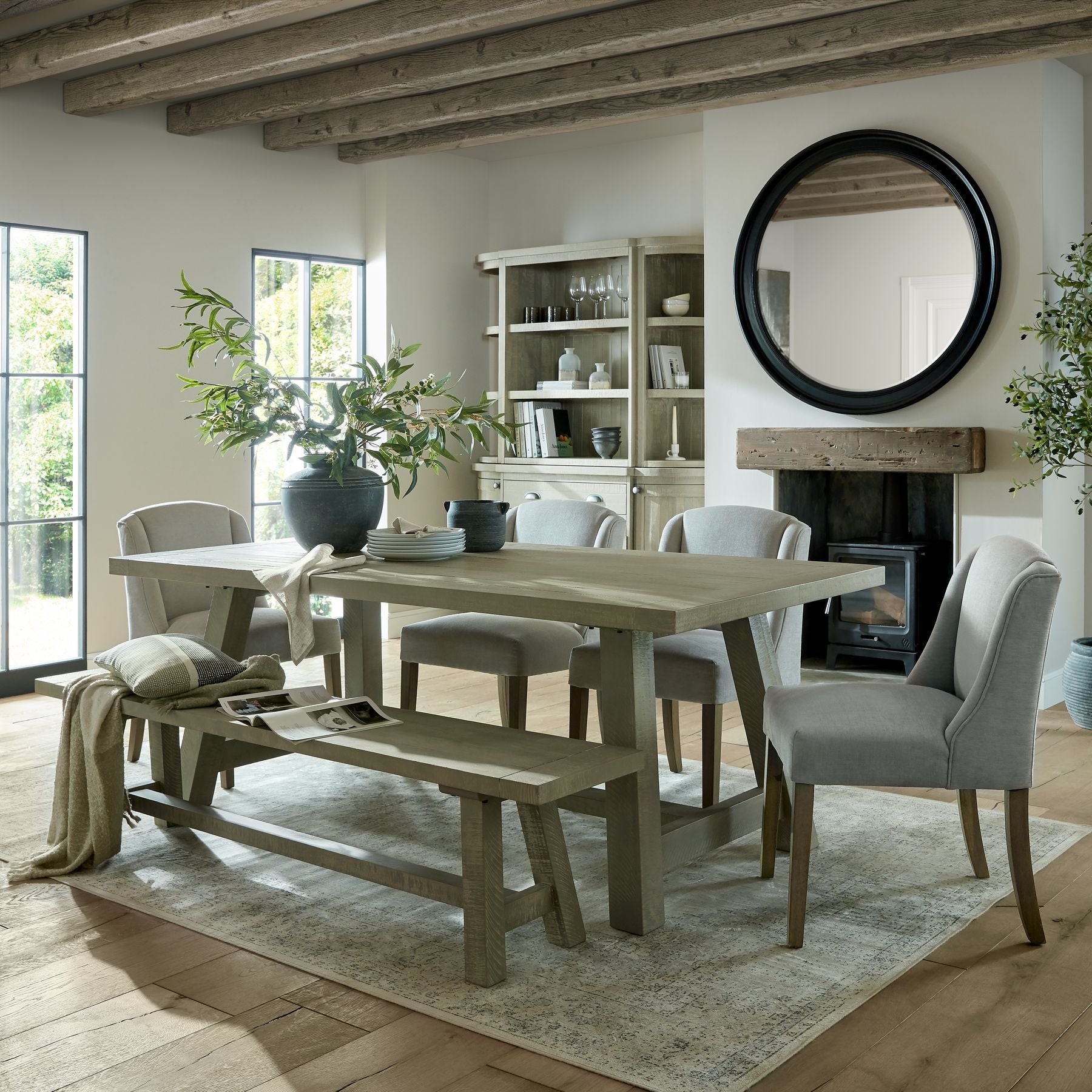 Rectangular dining table with a weathered finish, paired with soft gray upholstered chairs, set in a light-filled room.
