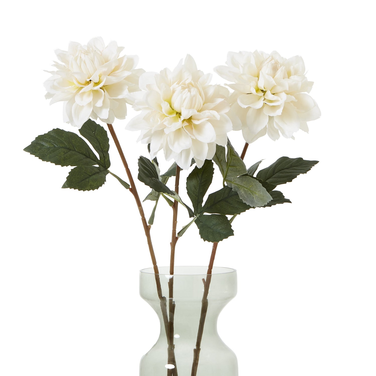 Three tall, white artificial dahlias with layered petals and green leaves in a clear vase, showcasing elegant and timeless floral decor.