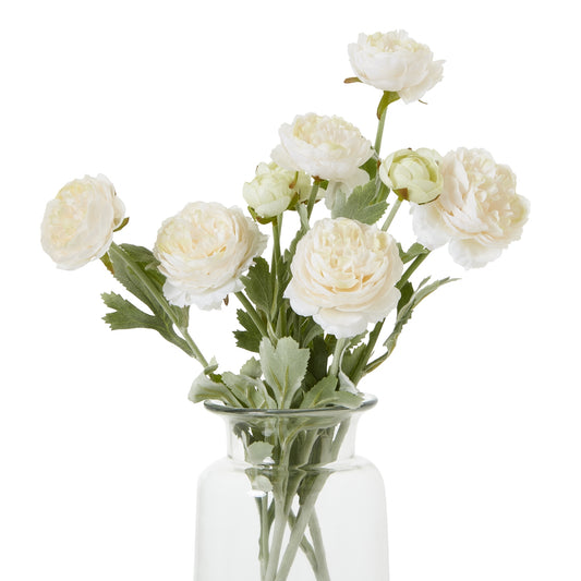 Lifelike apricot ranunculus with layered cream petals and green foliage, arranged in a clear glass vase for elegant decor.