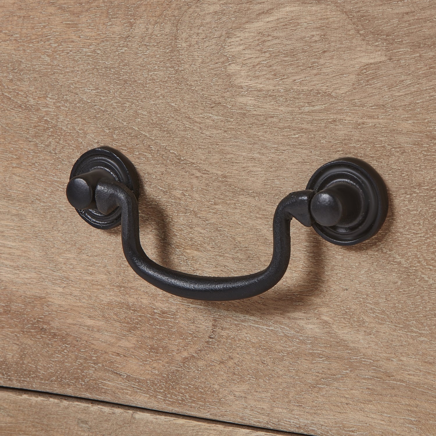 Close-up of a handcrafted drawer handle featuring black ironwork against a washed, bleached wood surface. Elegant and refined.