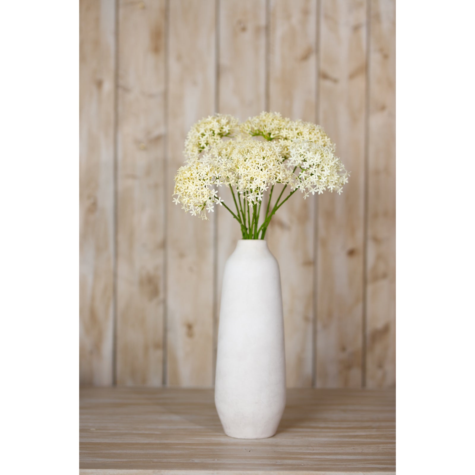 Elegant artificial Allium spray in delicate cream blooms, arranged in a tall, smooth white vase against a rustic wood backdrop.