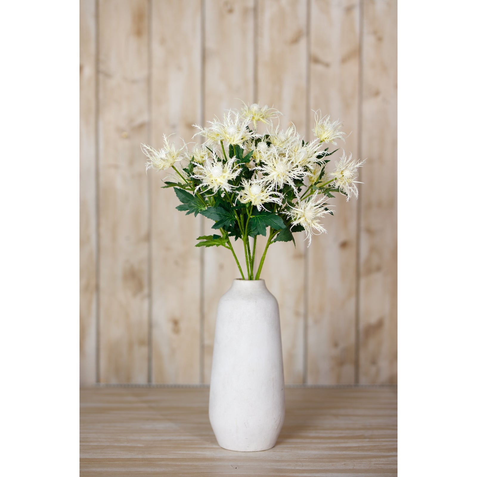 Cream-colored faux sea holly blooms arranged in a simple white vase, set against a rustic wooden background.
